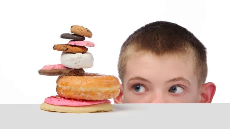 Menino observa vários doces: crianças devem evitar consumo de açúcar?