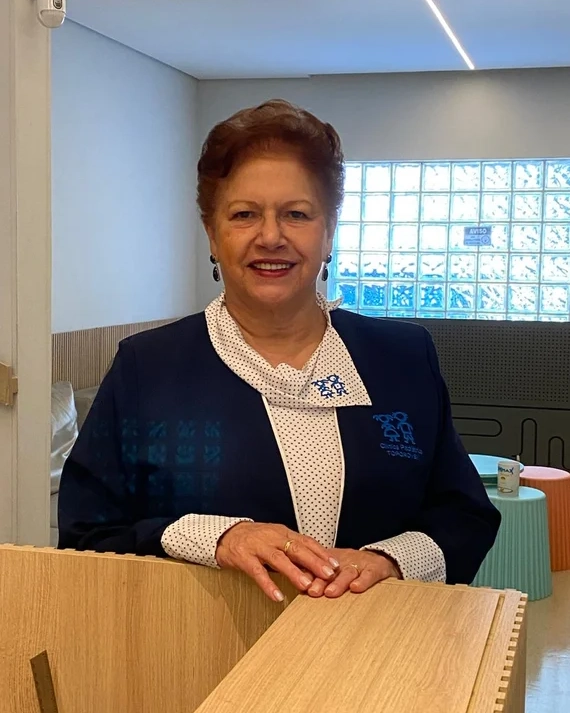 A administradora da clínica sorrindo atrás de um balcão: Lair Cleto Michalany